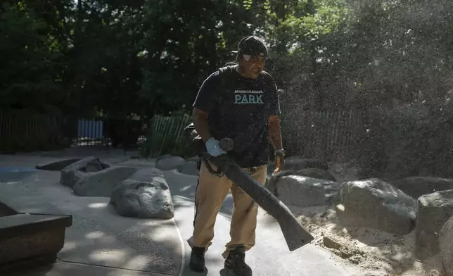 A park employee uses a sand blower to clear sand from a playground before opening it to children during a heatwave on Tuesday, June 24, 2025, in New York. (AP Photo/Olga Fedorova)