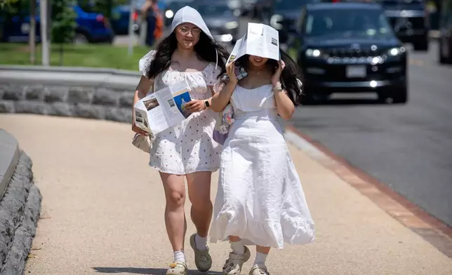 Visitors use brochures to shield themselves from the sun as they walk near the U.S. Capitol on an unseasonably hot day, Tuesday, June 24, 2025, in Washington. (AP Photo/Mark Schiefelbein)