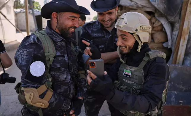 A member of the government security forces, right, laughs with fighters from the Kurdish-led Syrian Democratic Forces during a prisoner exchange in the Sheikh Maqsoud neighborhood of Aleppo, Syria, Monday, June 2, 2025. (AP Photo/Omar Albam)