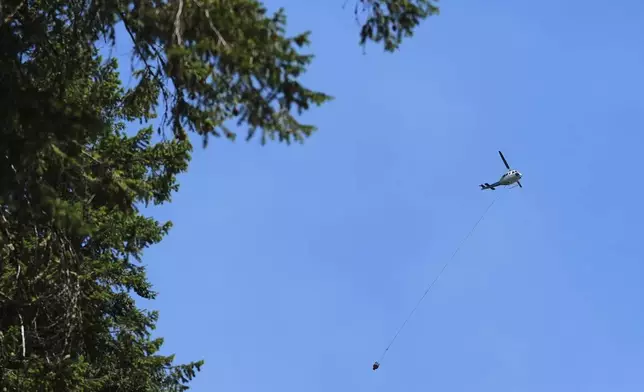 A firefighting helicopter flies over the scene of a wildfire the day after a shooter ambushed and killed multiple firefighters responding to the wildfire at Canfield Mountain Monday, June 30, 2025, in Coeur D'Alene, Idaho. (AP Photo/Lindsey Wasson)