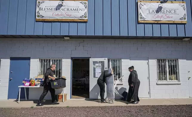 League of the Blessed Sacrament members Eric Faris, from left, Edward Seeley and Lisa Hezmalhalch gather up items displayed outside their thrift store as they prepare to close for the day, in Concho, Ariz., Saturday, June 21, 2025. (AP Photo/Roberto E. Rosales)