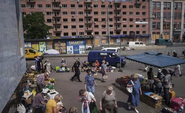 People shop at a street market near a building which was damaged by a Russian attack in Kyiv, Ukraine, on Thursday, July 10, 2025. (AP Photo/Evgeniy Maloletka)
