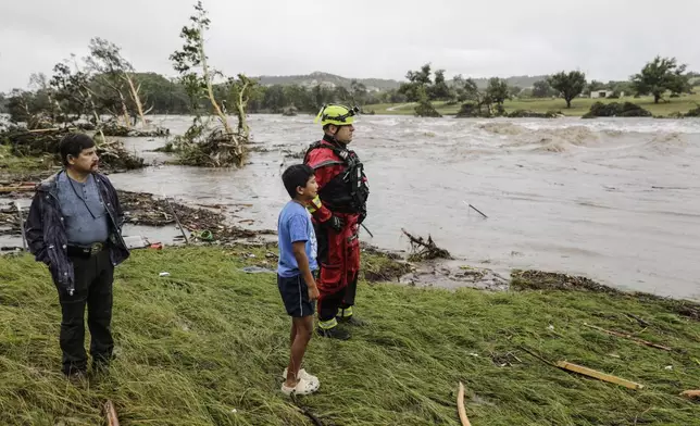Patricio Levesange, left, his grandson, 10-year-old Benjamin Levesange, center, and a Kerrville Fire Department first responder scan the banks of the Guadalupe River for people swept away by flooding on Friday, July 4, 2025, in Ingram, Texas. (Michel Fortier/The San Antonio Express-News via AP)