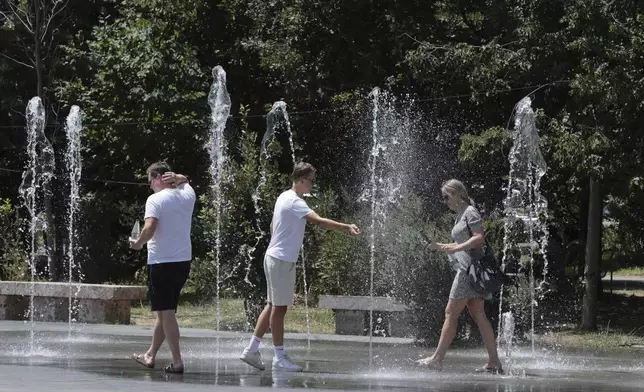 Pedestrians cool themselves in a fountain in central Tirana, Albania, during a heatwave on Friday, July 25, 2025. (AP Photo/Vlasov Sulaj)