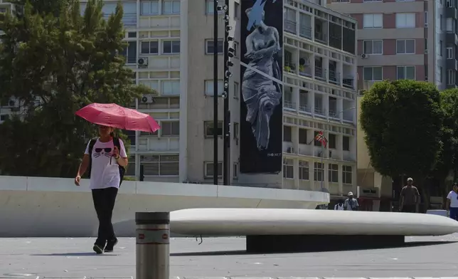 A woman uses an umbrella to protect herself from the sun during a hot day at Eleftherias square in central capital Nicosia, Cyprus, Friday, July 25, 2025. (AP Photo/Petros Karadjias)