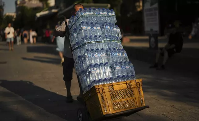 A man deliver plastic bottles of water to a popular restaurant on a hot summer day, in Istanbul, Turkey, Thursday, July 24, 2025. (AP Photo/Francisco Seco)