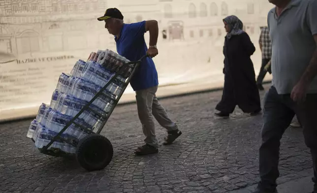 A man delivers plastic bottles of water to a local restaurant on a hot summer day at Eminonu district, in Istanbul, Turkey, Friday, July 25, 2025. (AP Photo/Francisco Seco)