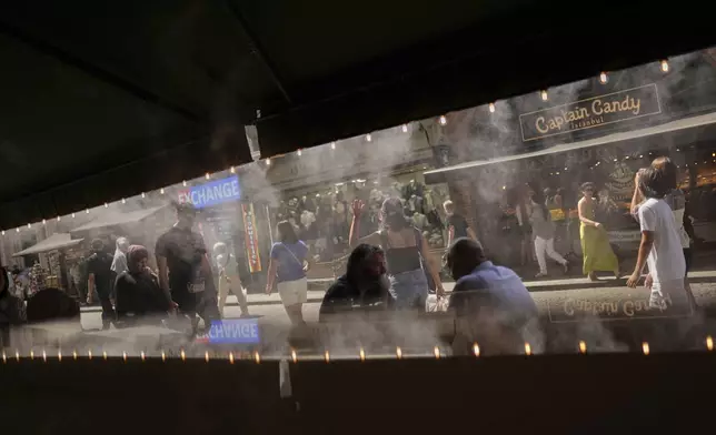 People walk past a coffee bar as water is sprayed to cool the area on a hot summer day, in Istanbul, Turkey, Friday, July 25, 2025. (AP Photo/Francisco Seco)