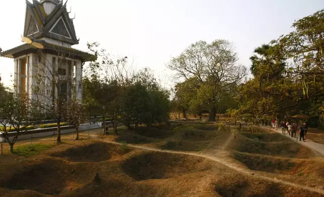 FILE - Visitors walk by the mass grave of the victims of the Khmer Rouge regime next to a memorial stupa filled with victims' skulls at the Choeung Ek killing field in Phnom Penh, Cambodia, Wednesday, Feb. 19, 2014. (AP Photo/Heng Sinith, File)