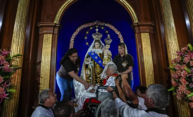 Church staff hold up Diablita dancer Berta Burgos, 101, in her wheelchair during a celebration of the Virgen de Carmen or Our Lady of Mount Carmel, Chile's patron saint, in La Tirana, Chile, Monday, July 14, 2025. (AP Photo/Esteban Felix)