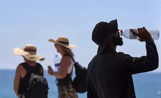 FILE - A tourist drinks water on a hot day at the beach in Barcelona, Spain, July 2, 2025. (AP Photo/Emilio Morenatti, File)