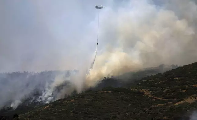 A helicopter drops water to extinguish a fire raging across a forested area in Odemis, near Izmir, Turkey, Friday, July 4, 2025. (Cengiz Malgir/Dia Photo via AP)