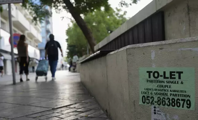 People walk past a concrete bench plastered with advertisements for inexpensive, partitioned housing in Dubai, United Arab Emirates, Friday, July 4, 2025. (AP Photo/Altaf Qadri)