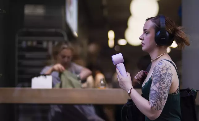A woman uses a handheld fan in hot weather in Covent Garden, in London, Monday, June 30, 2025. (AP Photo/Alberto Pezzali)