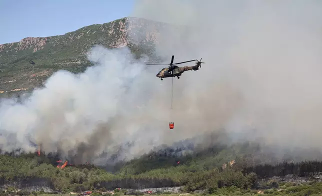 A helicopter sprays water to extinguish a fire in Seferihisar, near Izmir, Turkey, Monday, June 30, 2025. (Cengiz Malgir/Dia Photo via AP)