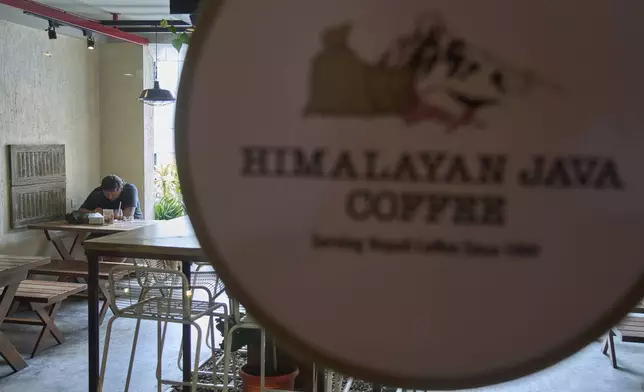 A person checks his mobile phone while drinking coffee at a cafe in Kathmandu, Nepal, Tuesday, June 10, 2025. (AP Photo/Niranjan Shrestha)