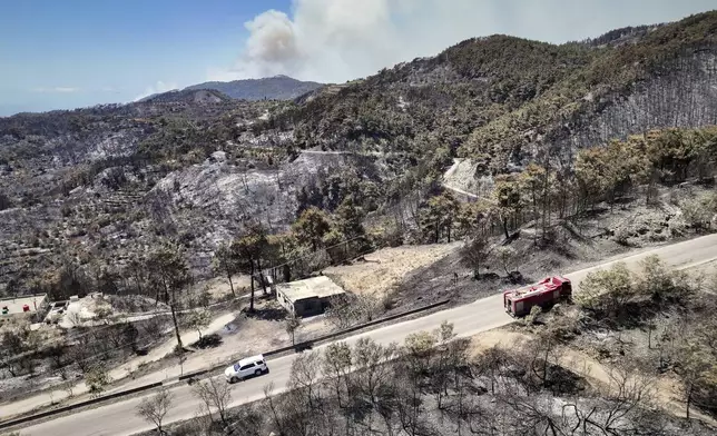 A fire truck sits on a road amid a wide stretch of burned hills, as smoke rises into the sky in the background on the fifth consecutive day of a wildfire near the town of Rabia, in Syria's Latakia countryside, Monday, July 7, 2025. (AP Photo/Ghaith Alsayed)