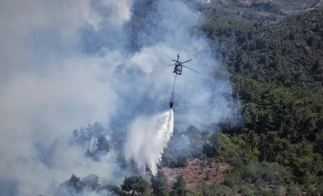 A Turkish helicopter drops water on the flames as it helps fight a wildfire near the town of Rabia, in Syria's Latakia countryside, early Monday, July 7, 2025. (AP Photo/Ghaith Alsayed)
