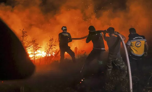 Emergency responders with the Syrian Civil Defense, known as the White Helmets, work to extinguish a wildfire near the town of Rabia, in Syria's Latakia countryside, early Monday, July 7, 2025. (AP Photo/Ghaith Alsayed)