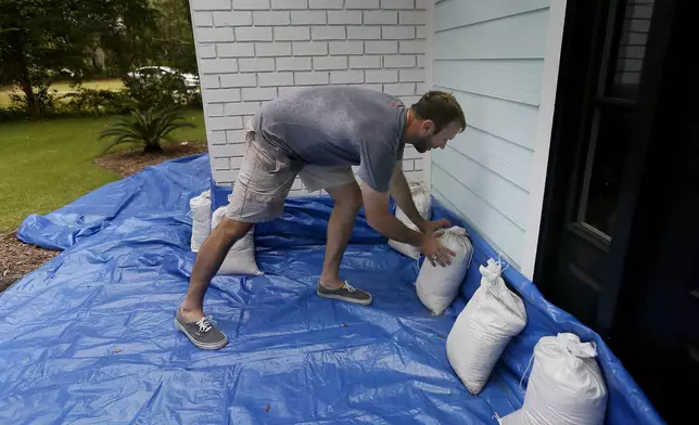 FILE - Stewart Thomason places sandbags that he used for previous hurricanes and tarp to prevent the flooding from rain at his home on the Isle of Palms, S.C. ahead of Hurricane Florence, on Wednesday, Sept. 12, 2018. (Grace Beahm Alford/The Post And Courier via AP,File)