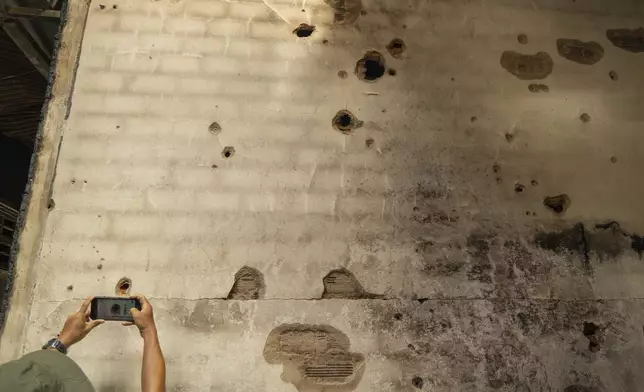 A man takes photos of shrapnel holes in a bombed building in O'Smach, Oddar Meanchey in Cambodia on Wednesday, July 30, 2025. (AP Photo/Anton L. Delgado)