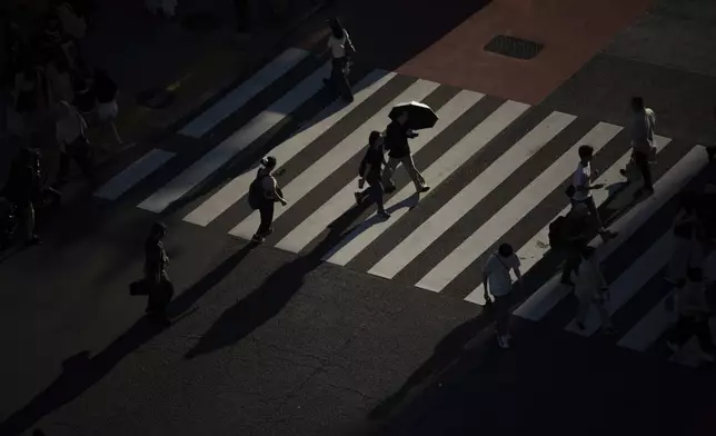 Pedestrians walk across a crossing in Tokyo, Monday, July 21, 2025. (AP Photo/Louise Delmotte)
