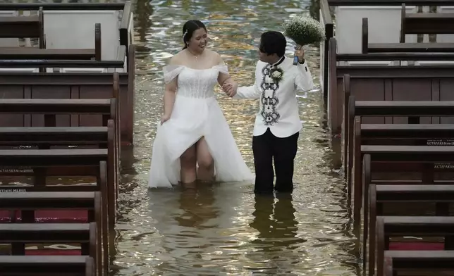 Newlyweds Jade Rick Verdillo right, and Jamaica walk hand in hand during their wedding at the flooded Barasoain church in Malolos, Bulacan province, Philippines on Tuesday, July 22, 2025. (AP Photo/Aaron Favila)