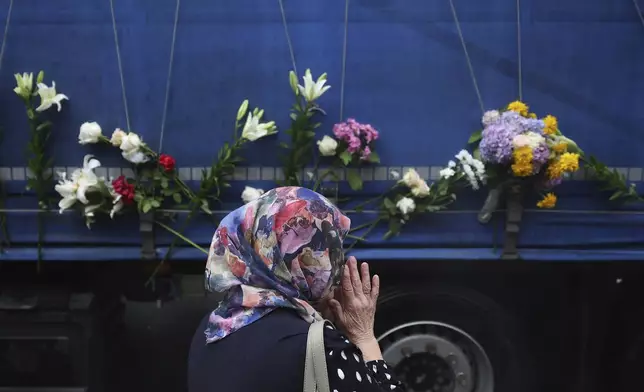A women prays next to a truck carrying remains of the identified victims of the 1995 Srebrenica massacre to the Memorial centre in Potocari, where they will be buried on July 11, in Sarajevo, Bosnia, Wednesday, July 9, 2025. (AP Photo/Armin Durgut)