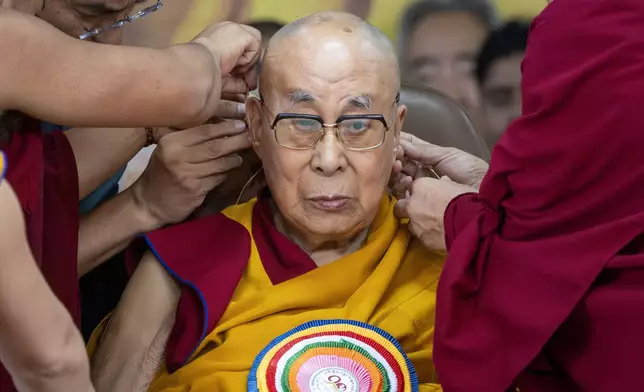 Attendant monks help put a microphone around Tibetan spiritual leader the Dalai Lama's head during his 90th birthday celebrations at the Tsuglakhang temple in Dharamshala, India, Sunday, July 6, 2025.(AP Photo/Ashwini Bhatia)