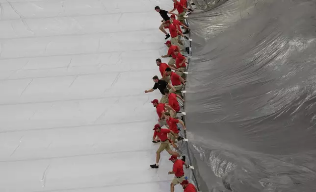 Members of the grounds crew remove a tarp from the field after a rain delay before a baseball game between the Cincinnati Reds and the Miami Marlins in Cincinnati, Monday, July 7, 2025. (AP Photo/Carolyn Kaster)