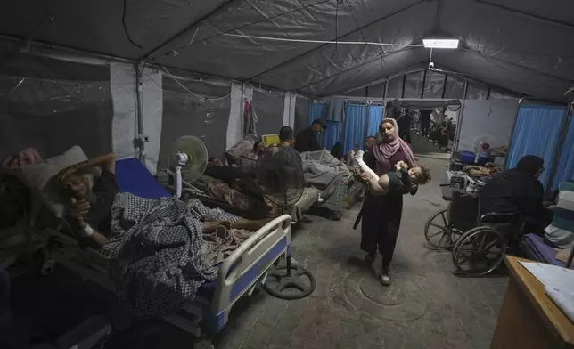 A mother carries her child into a patient treatment tent set up in the yard of Shifa Hospital in Gaza City, Friday, July 4, 2025. (AP Photo/Jehad Alshrafi)