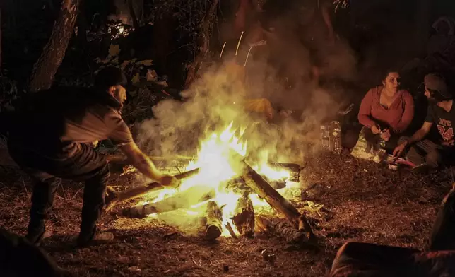 Migrants gather by a campfire in the Ecault forest, northern France, Friday, July 4, 2025. (AP Photo/Nicolas Garriga)
