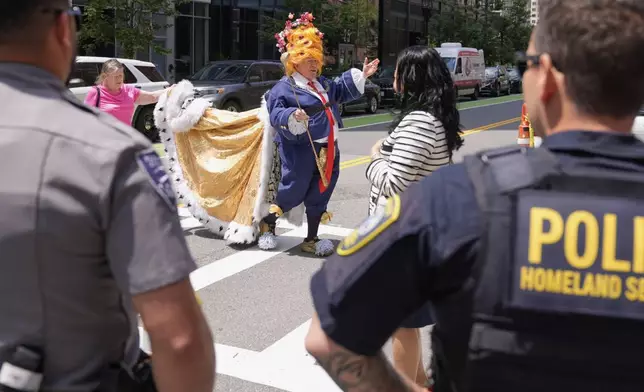 Law enforcement watch as an actor dressed in a costume, who identified himself as "the real mad king", walks toward protestors outside the Moakley Federal Courthouse, where Harvard University appeared to challenge $2.6 billion in funding cuts by the Trump administration, Monday, July 21, 2025, in Boston. (AP Photo/Charles Krupa)
