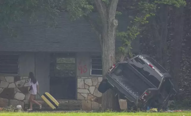 A person pulls luggage at Camp Mystic along the banks of the Guadalupe River after a flash flood swept through the area Sunday, July 6, 2025, in Hunt, Texas. (AP Photo/Julio Cortez)