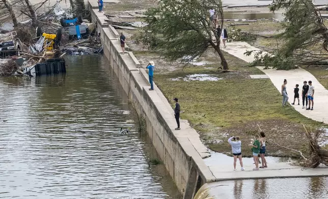 Onlookers walk along the banks of the Guadalupe River in Louise Hays Park, Saturday, July 5, 2025, in Kerrville, Texas. (AP Photo/Rodolfo Gonzalez)
