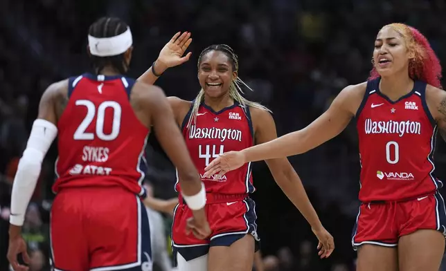 Washington Mystics guard Brittney Sykes (20) is greeted by forward Kiki Iriafen (44) and forward Shakira Austin (0) as they celebrate a lead over the Seattle Storm late during the second half of a WNBA basketball game Sunday, July 13, 2025, in Seattle. (AP Photo/Lindsey Wasson)