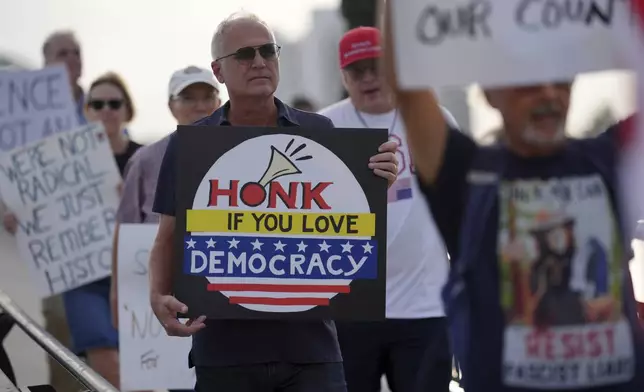 People hold signs as they participate in a pro-democracy, anti-Trump protest outside Trump's Mar-a-Lago estate in Palm Beach, Fla., as part of the "Good Trouble Lives On" national day of action, Thursday, July 17, 2025. (AP Photo/Rebecca Blackwell)