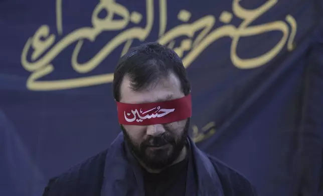 A Hezbollah supporter who lost his sight in a pager attack carried out by Israel on Sept. 17, 2024, covers his eyes with a red headband inscribed with the name "Hussein" during Ashoura, the Shiite Muslim commemoration marking the 7th-century death of Imam Hussein, the grandson of the Prophet Muhammad, in the southern suburbs of Beirut, Lebanon, Sunday, July 6, 2025. (AP Photo/Hassan Ammar)