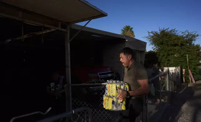 Gerardo Sanchez, an outreach coordinator with the immigrant and farmworker justice group TODEC, helps deliver bottled water to mobile home residents in Oasis, Calif., Monday, April 14, 2025. (AP Photo/Jae C. Hong)