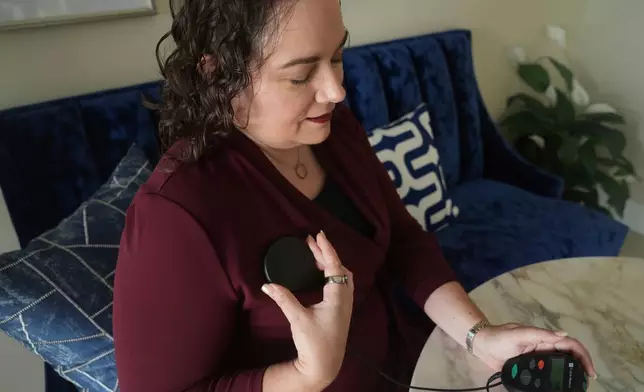 Brandy Ellis charges a pacemaker-like device that was installed in her chest as part of an experimental treatment for depression, on Thursday, July 24, 2025, in Delray Beach, Fla. (AP Photo/Marta Lavandier)