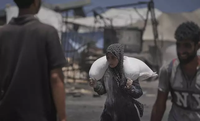 Palestinians carry sacks of flour unloaded from a humanitarian aid convoy that reached Gaza City from the northern Gaza Strip, Tuesday, July 22, 2025. (AP Photo/Jehad Alshrafi)