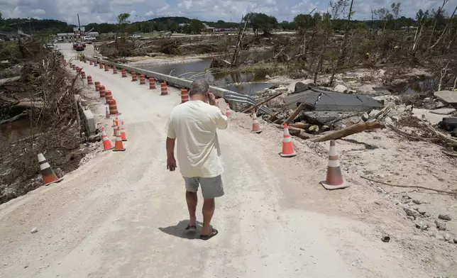 Resident Paul Snyder walks down the road to check out the condition of the bridge along the Guadalupe River after flooding in Ingram, Texas on Wednesday , July 9, 2025. (AP Photo/Gerald Herbert)