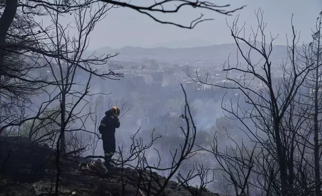 A firefighter stands among burned trees during a wildfire at the Polytechnic University of Athens as the Greek capital is seen in the background, Monday, July 28, 2025. (AP Photo/Thanassis Stavrakis)