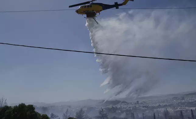 A firefighting helicopter drops water to extinguish a fire at the Polytechnic University of Athens as the Greek capital is seen in the background on Monday, July 28, 2025. (AP Photo/Thanassis Stavrakis)