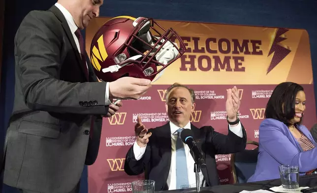 FILE - Washington Commanders controlling owner Josh Harris, center, is passed a helmet to sign next to District of Columbia Mayor Muriel Bowser, right, after announcing a new home for the NFL football team on the site of the old RFK Stadium, Monday, April 28, 2025, at the National Press Club in Washington. (AP Photo/Jacquelyn Martin, File)