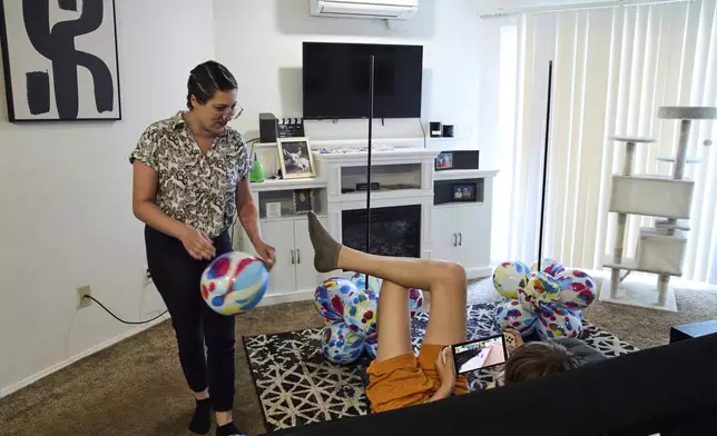 Havalah Hopkins, a single mother who lives in government-subsidized housing with her teenage son, talks with her son as she blows up balloon displays for his birthday, Thursday, July 10, 2025, at their apartment in Woodinville, Wash. (AP Photo/Lindsey Wasson)