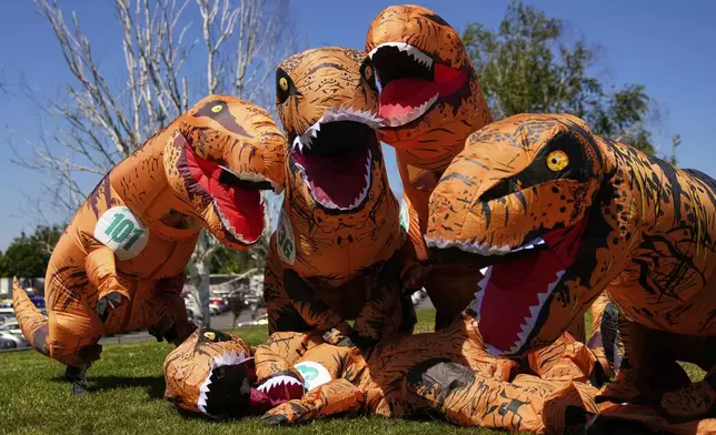 From left, friends Carmen Alvarado, Donaji Torres, Mazay Jimenez and Hector Hernandez pose as pretend to eat their deflated T-Rex friend Joselyne Rivera, on the ground, during the "T-Rex World Championship Races" at Emerald Downs, Sunday, June 29, 2025, in Auburn, Wash. (AP Photo/Lindsey Wasson)