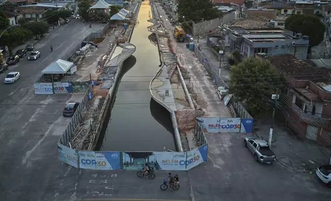 FILE - People ride bikes near signage for the upcoming COP30 U.N. Climate Summit in Belem, Brazil, March 23, 2025. (AP Photo/Jorge Saenz, File)