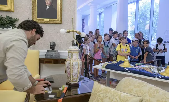 While a group of children look on, Luke Boorady works with a lamp during work to transition a replica of the White House Oval Office from the days of former President Joe Biden with President Donald Trump's decor, at the White House Historical Association in Washington, Wednesday, July 23, 2025. (AP Photo/Rod Lamkey, Jr.)