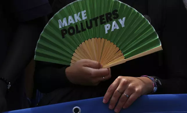 An activist holds a fan that reads "make polluters pay" as they demonstrate outside the International Court of Justice ahead of an advisory opinion on what legal obligations nations have to address climate change and which consequences they may face if they don't, on Wednesday, July 23, 2025, in The Hague, Netherlands. (AP Photo/Peter Dejong)